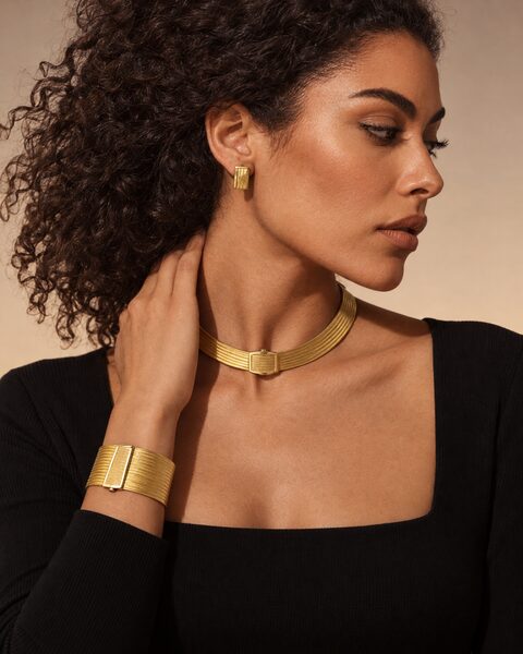 Frau in Schwarz mit Halsreif und breitem Armband aus geflochtenem Gelbgold